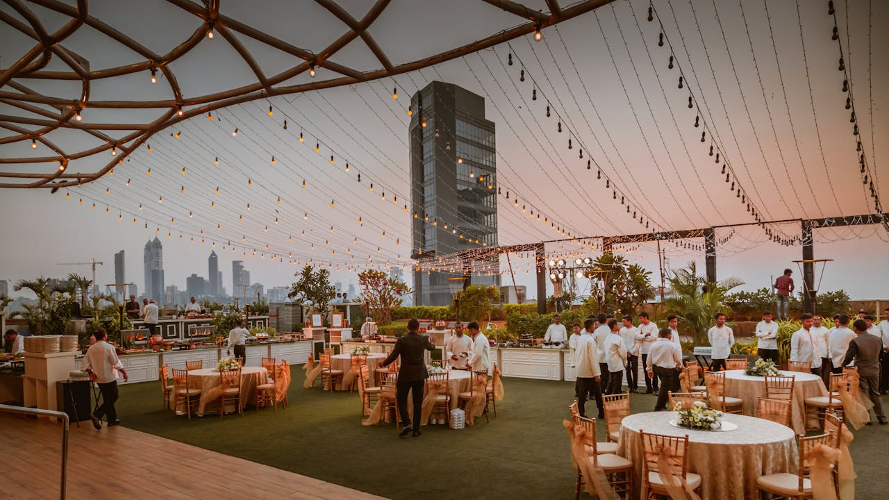 Elegant rooftop event with tables and lights set against Mumbai skyline at sunset, India.